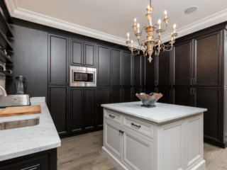 Custom built kitchen pantry featuring dark stained wood on inset cabinets with recessed doors. This pantry also features a white kitchen island with doors and drawers and all of the cabinetry is decorated with Top Knobs hardware